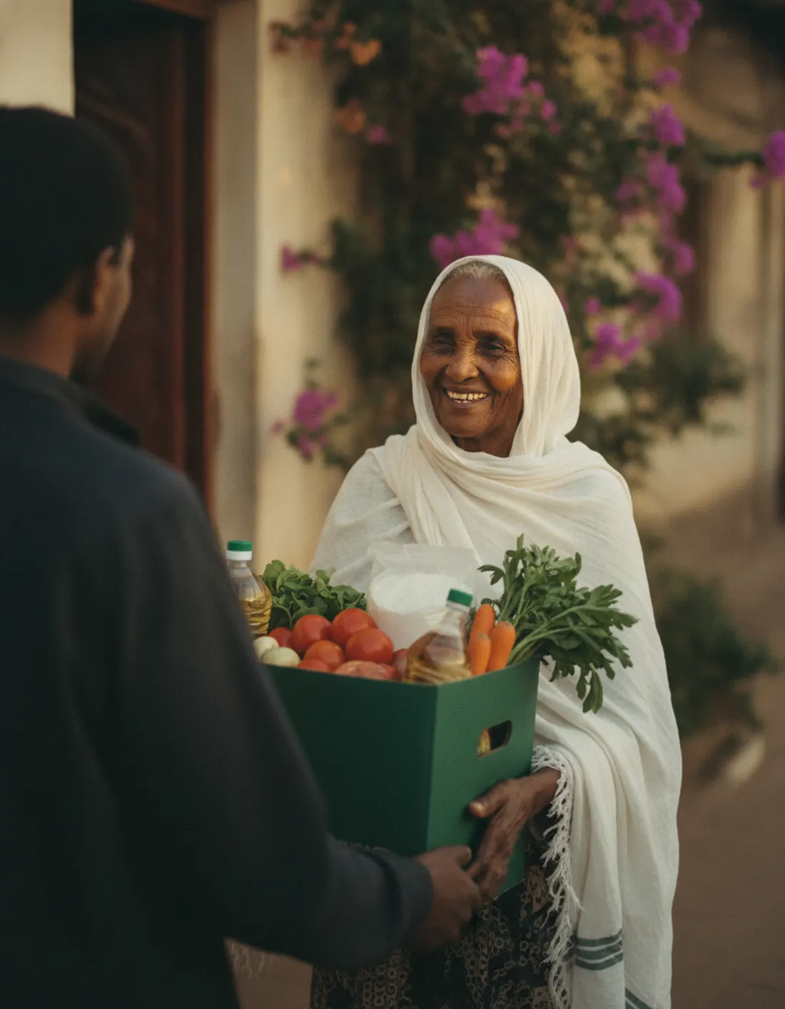An Ethiopian grandmother in a white netela smiling as she receives a green Adera grocery box at her door